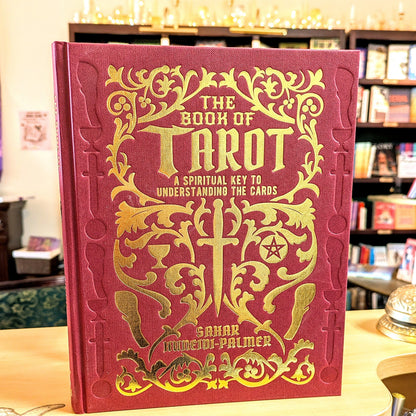 Red book titled 'The Book of Tarot' with gold text and designs on a table.