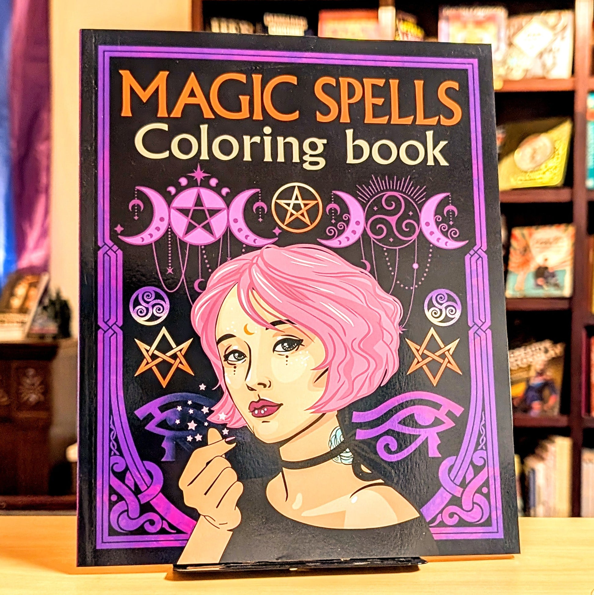 Coloring book titled 'Magic Spells' with a cover featuring a woman with pink hair and wiccan symbols.