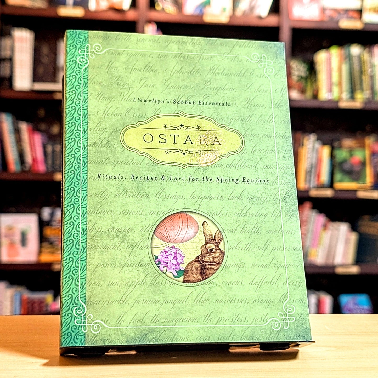 Green book titled 'Ostara' with rabbit and mushroom illustration on a bookshelf background