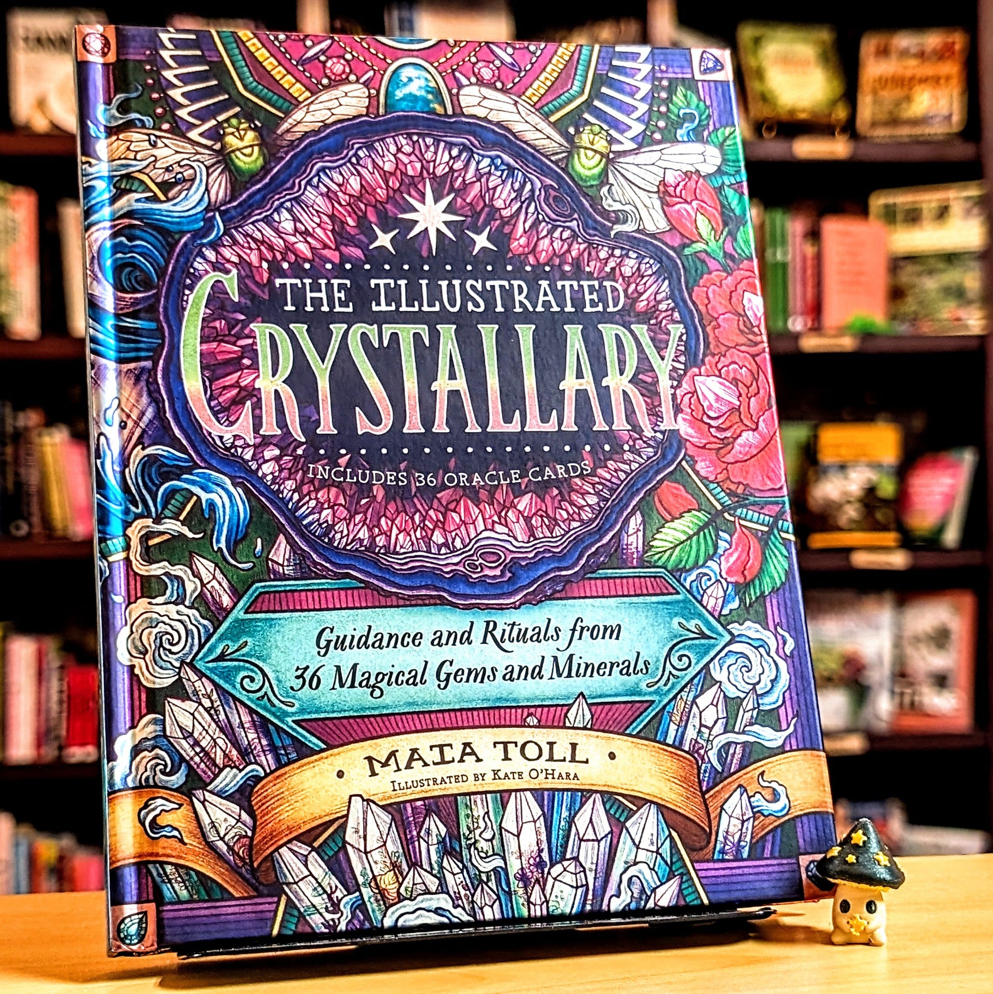 Colorful book titled 'The Illustrated Crystallary' on a wooden surface with a blurred bookshelf background.