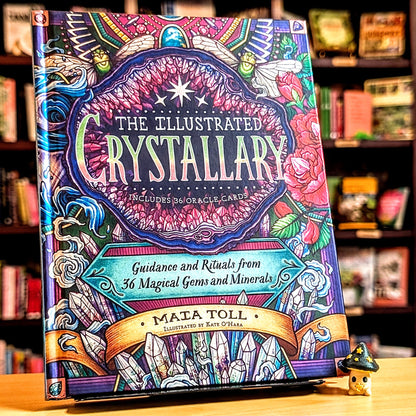 Colorful book titled 'The Illustrated Crystallary' on a wooden surface with a blurred bookshelf background.