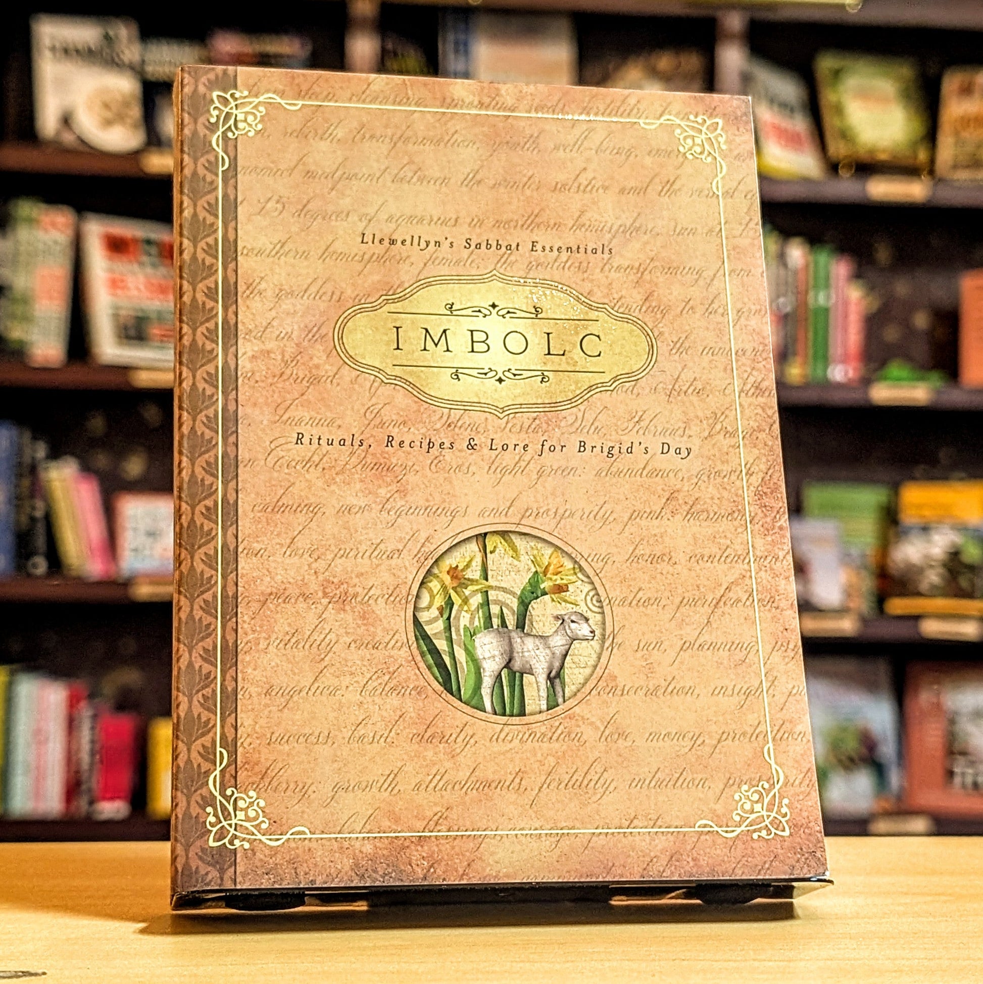 Book titled 'Imbolc' with a goat illustration on a wooden surface with a bookshelf background.