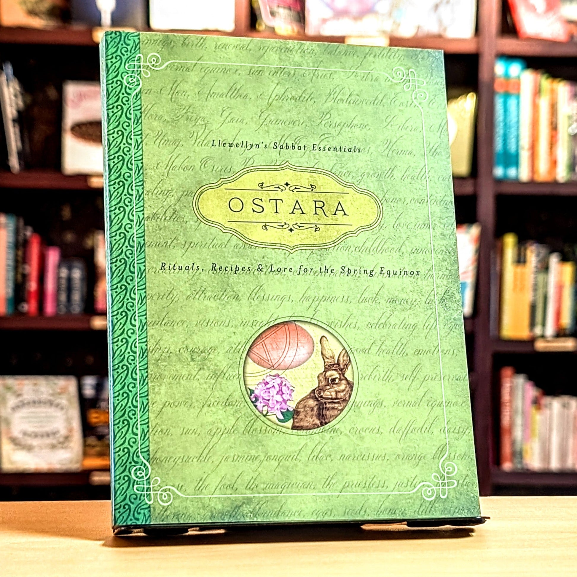 Green book titled 'Ostara' with rabbit and flower illustration on a bookshelf background