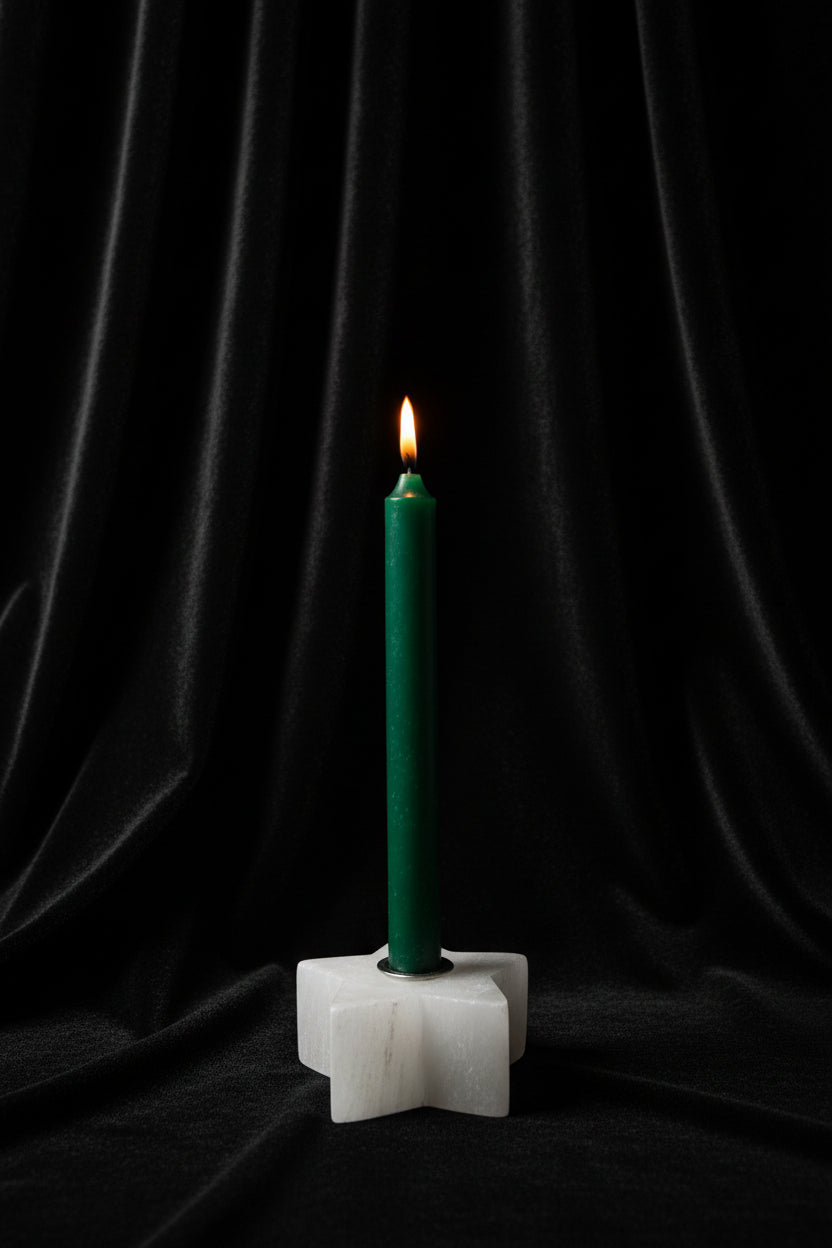 A green taper candle standing upright in a white star-shaped holder against a plain white background.