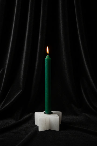 A green taper candle standing upright in a white star-shaped holder against a plain white background.