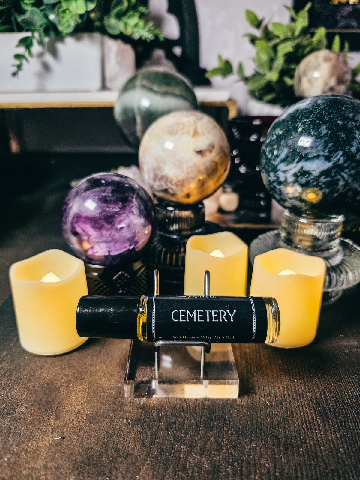 Candle with 'Cemetery' label on a stand, surrounded by decorative spheres and candles on a wooden surface.