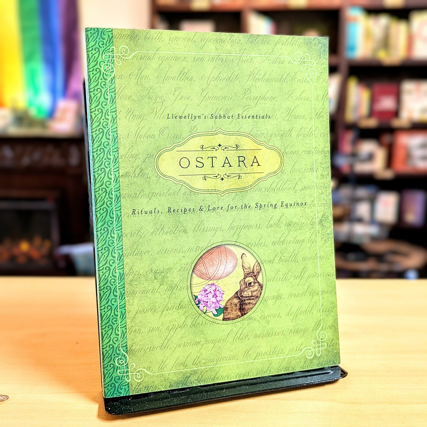 Green book titled 'Ostara' with rabbit and flower illustration on a wooden surface.