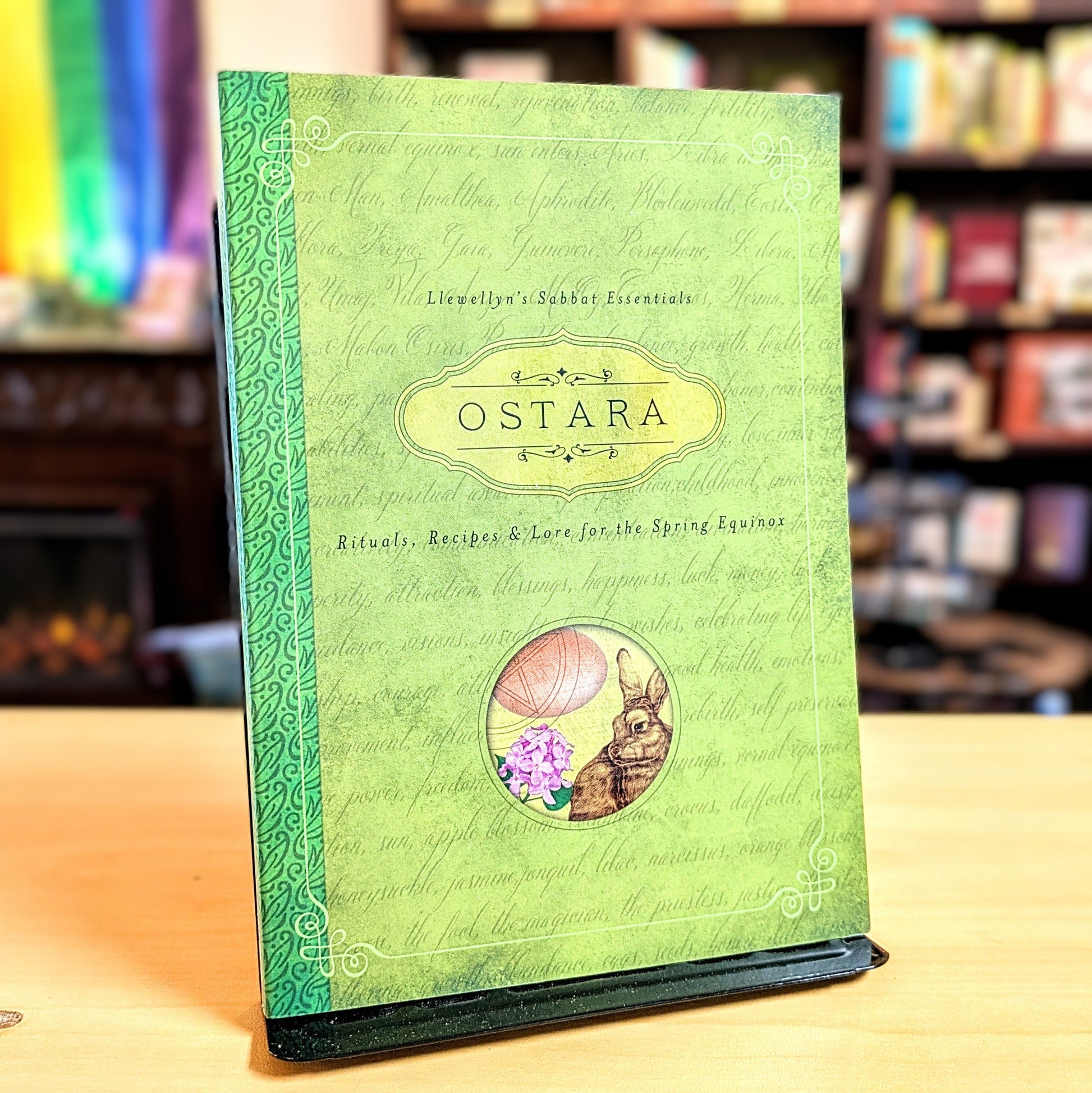 Green book titled 'Ostara' with rabbit and flower illustration on a wooden surface.