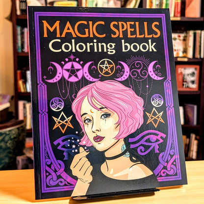 Coloring book titled 'Magic Spells' with an illustration of a person with pink hair on a table.