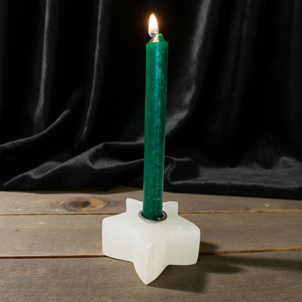A lit green taper candle standing in a white star-shaped holder on a rustic wooden surface against a dark gray background.