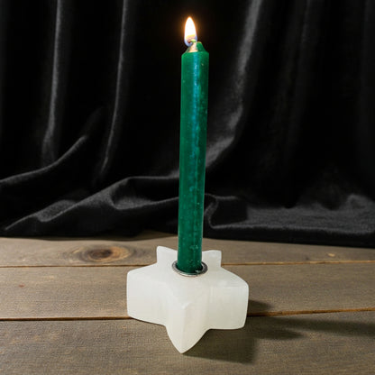 A lit green taper candle standing in a white star-shaped holder on a rustic wooden surface against a dark gray background.