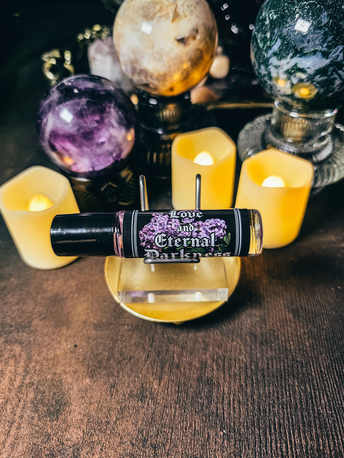 Candle with a label 'Love and Eternal Darkness' in front of crystal balls and candles on a wooden surface.