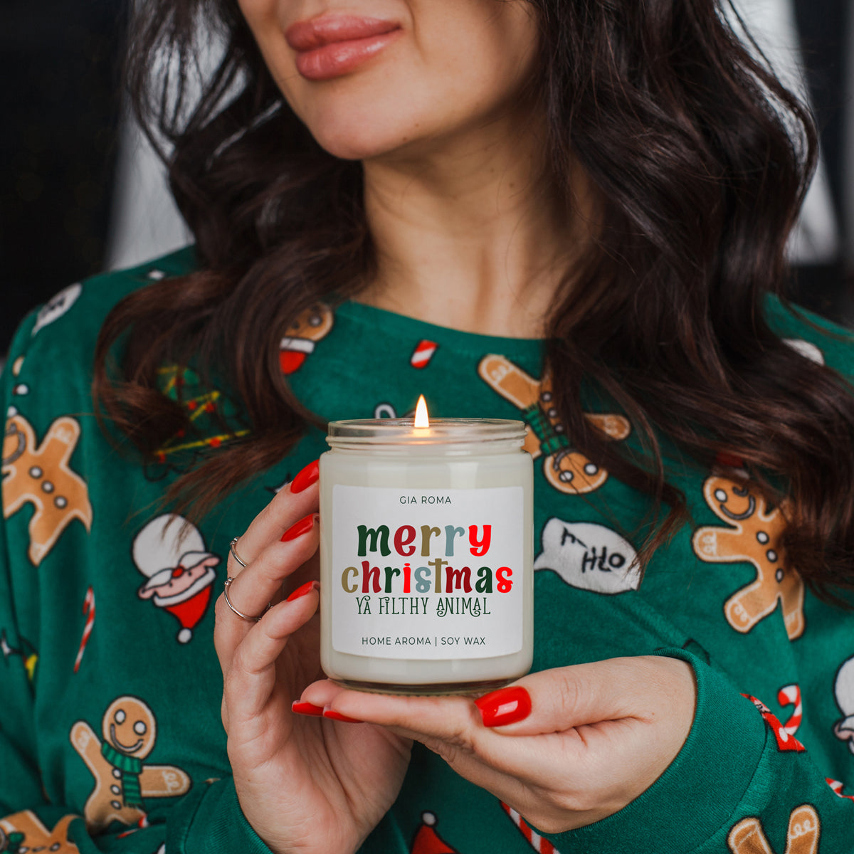 Person holding a lit candle with a 'merry christmas ya filthy animal' label, wearing a festive sweater.