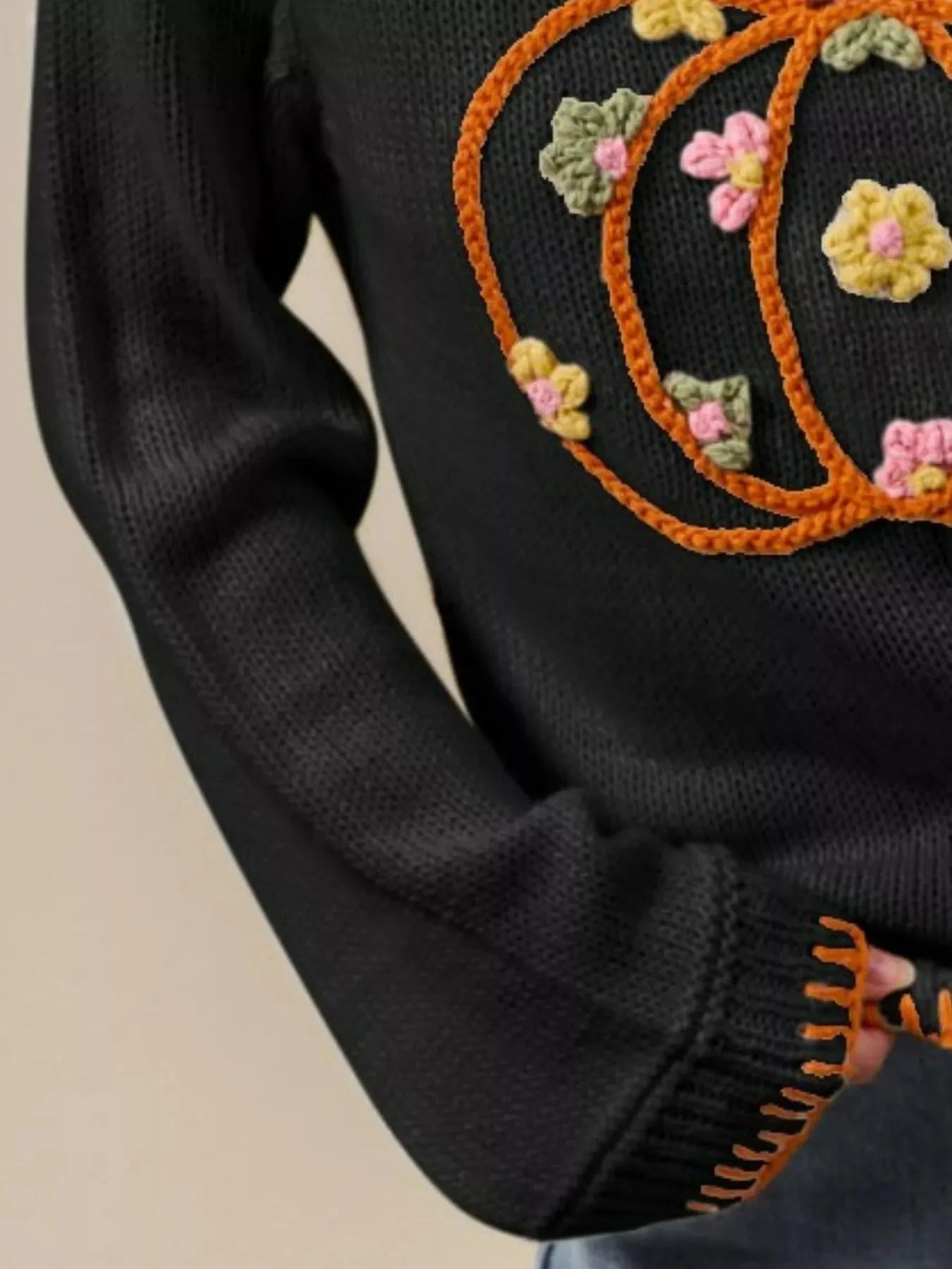Black sweater with orange and multicolor floral embroidery on a beige background