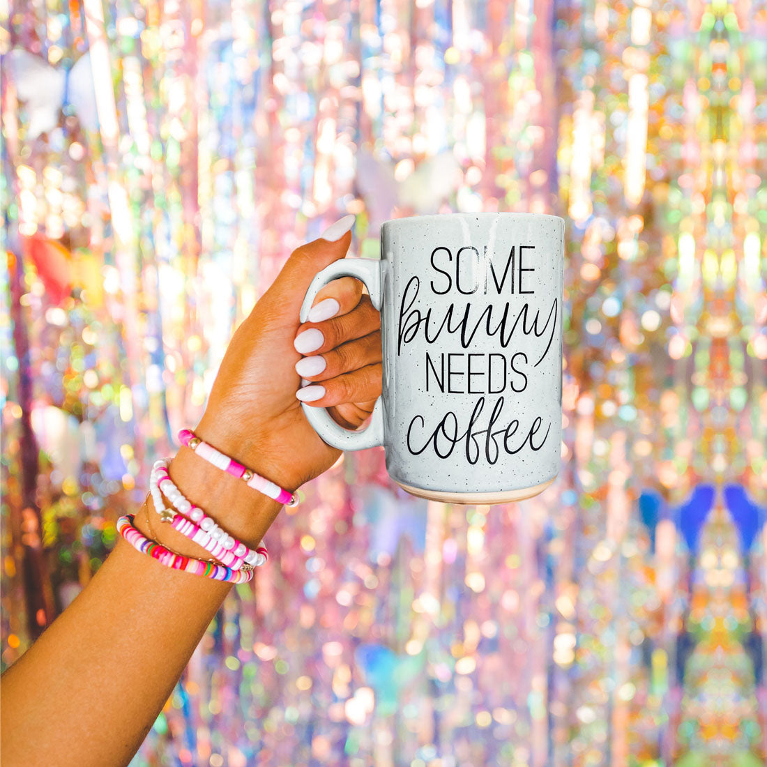 Hand holding a mug with 'Some bunny needs coffee' text against a colorful, blurred background