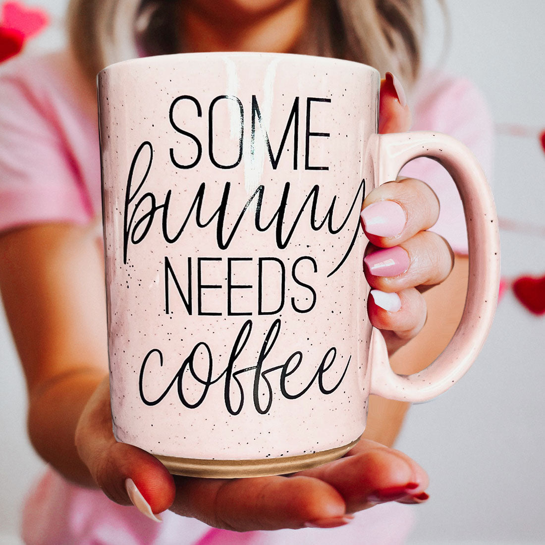 Person holding a pink mug with 'Some bunny needs coffee' text