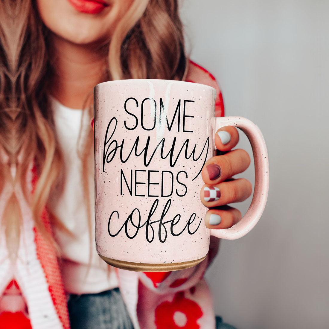 Person holding a pink mug with 'Some bunny needs coffee' text