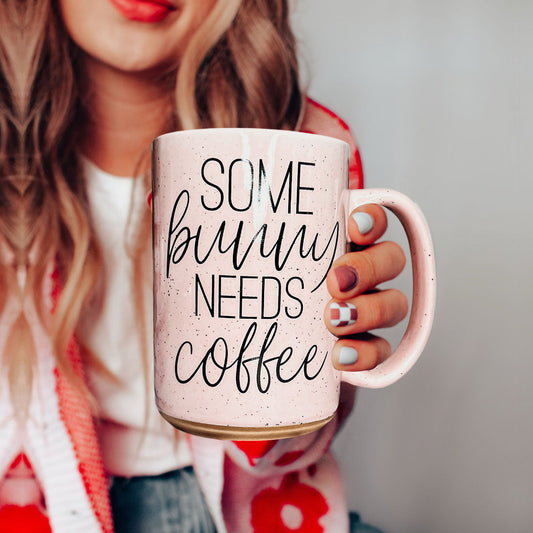 Person holding a pink mug with 'Some bunny needs coffee' text
