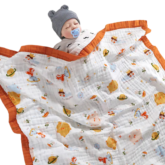 Baby sleeping under a patterned blanket with orange trim on a white background