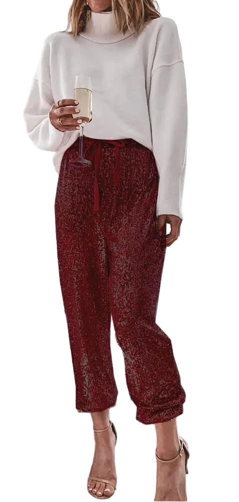 Woman in a white sweater and red pants standing in a living room with a Christmas tree.