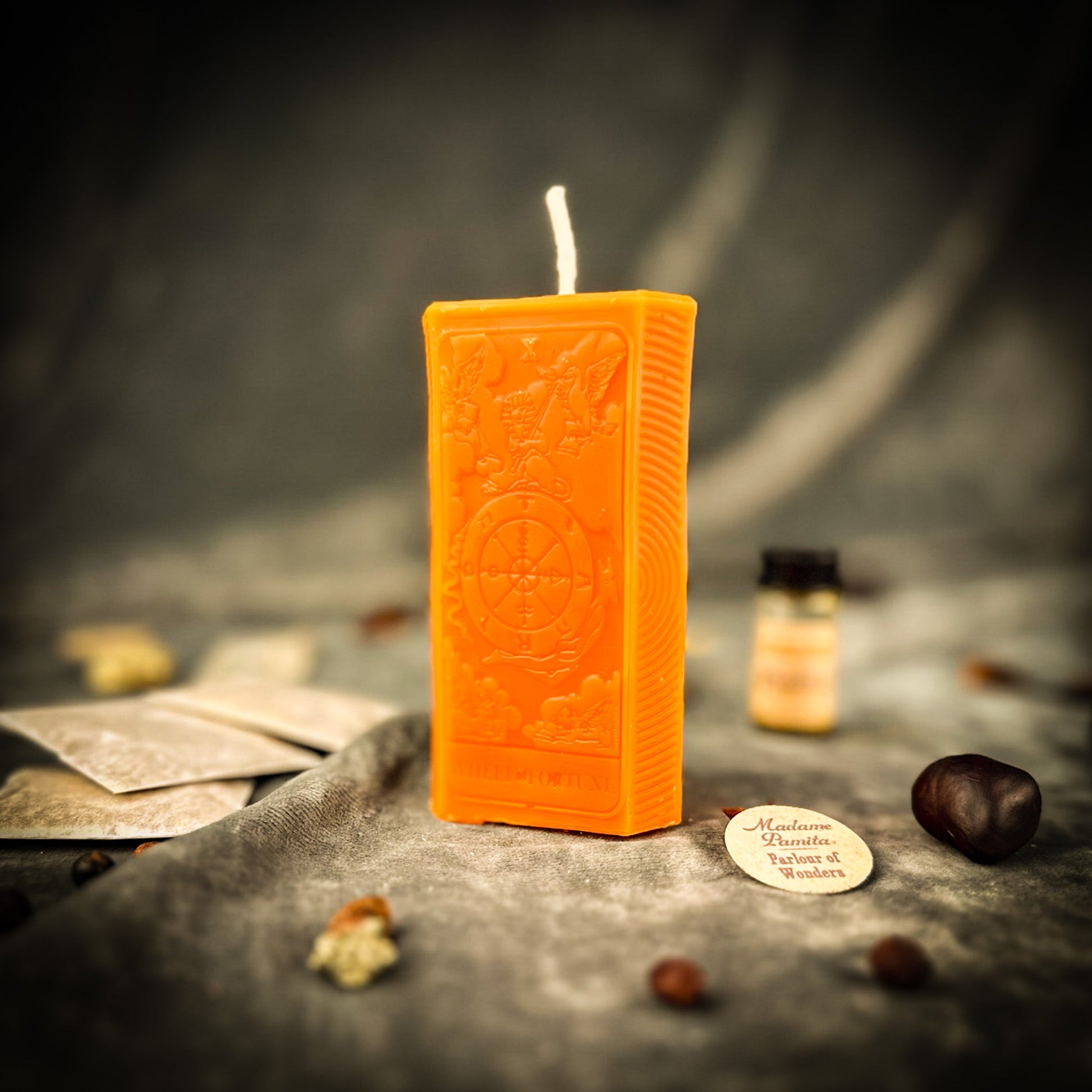 Orange rectangular candle with intricate design on a dark surface with blurred background