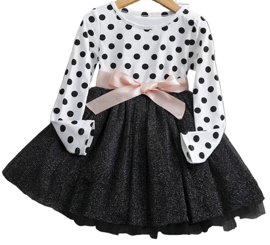 Polka dot blouse with a pink bow and black pleated skirt on a wooden surface.