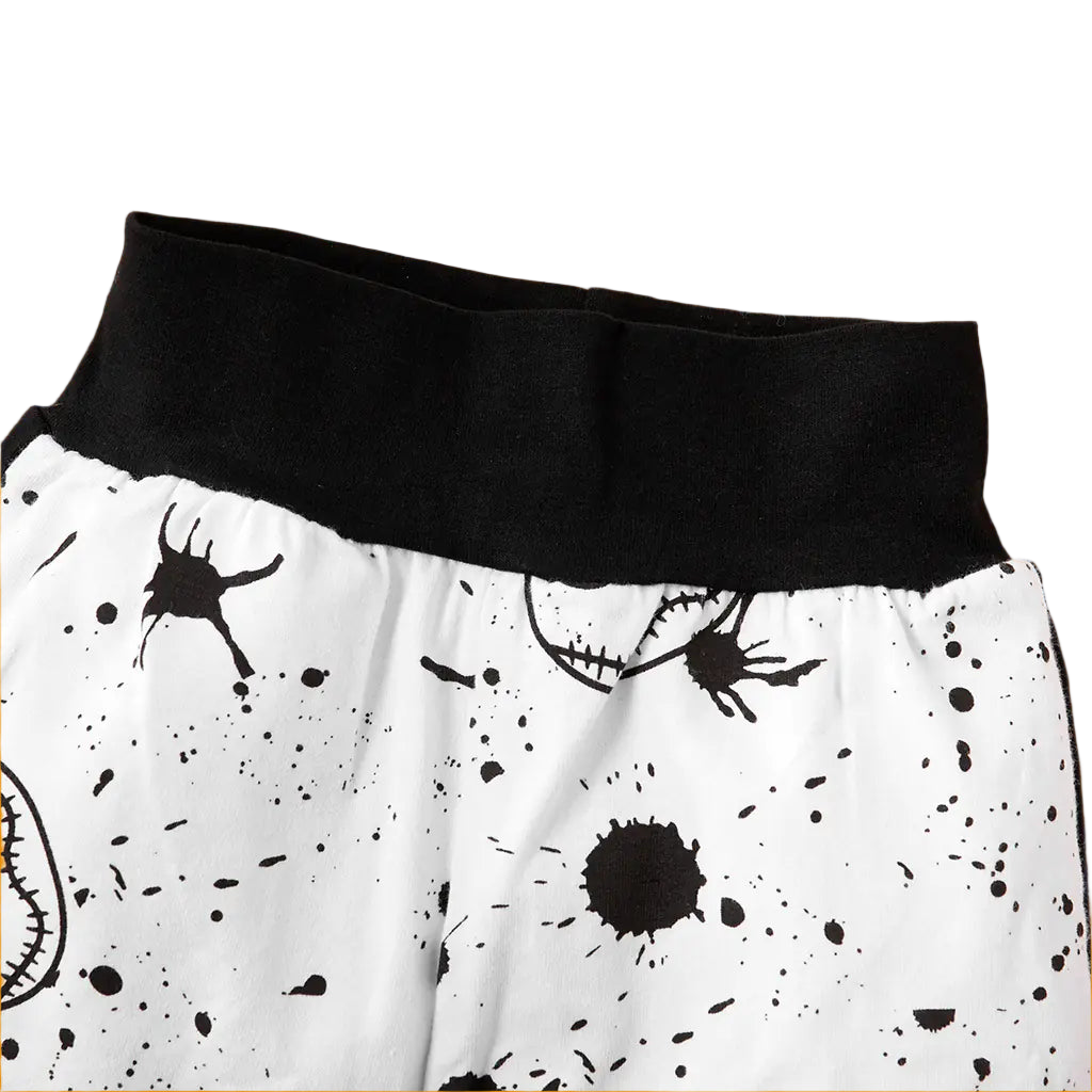Close-up of a black waistband and white pants with black splatter patterns on a beige background