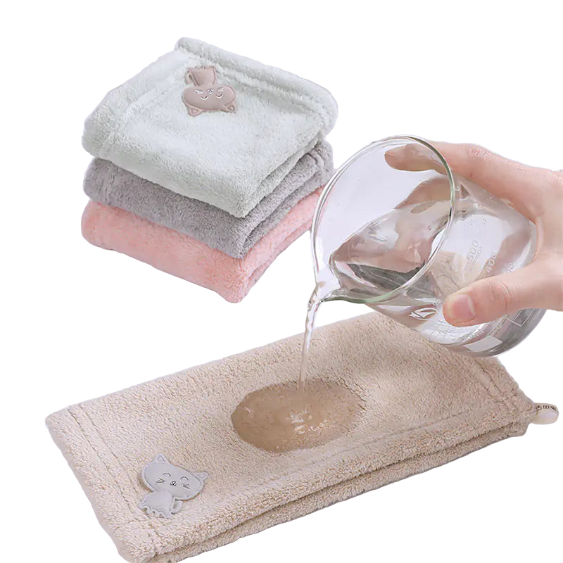 Towels with cat-shaped decorations on a white surface, with a glass of water being poured onto one towel.