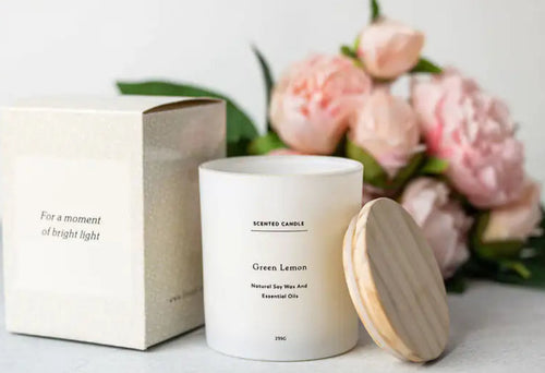 Candle with wooden lid and packaging on a light surface with flowers in the background