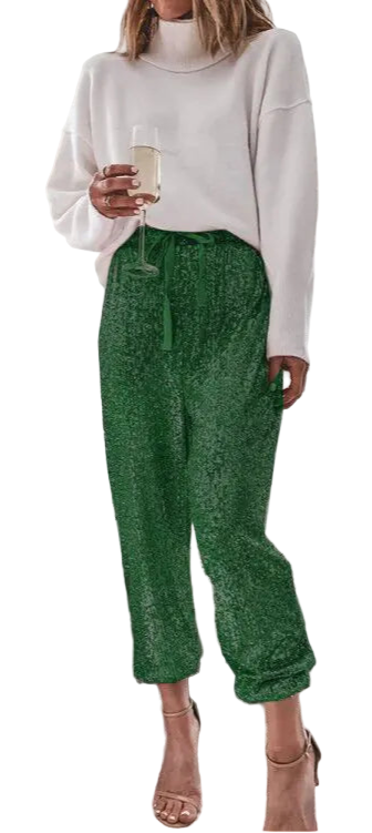 Woman in a white sweater and green pants standing in a living room with a Christmas tree.