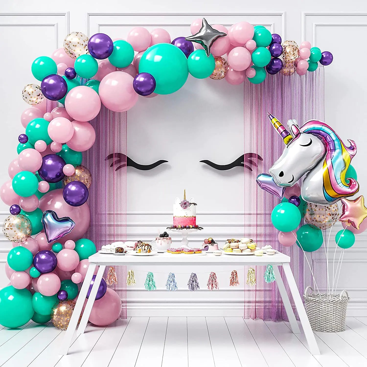 Colorful balloon arch with a unicorn balloon above a dessert table in a room with decorative walls.