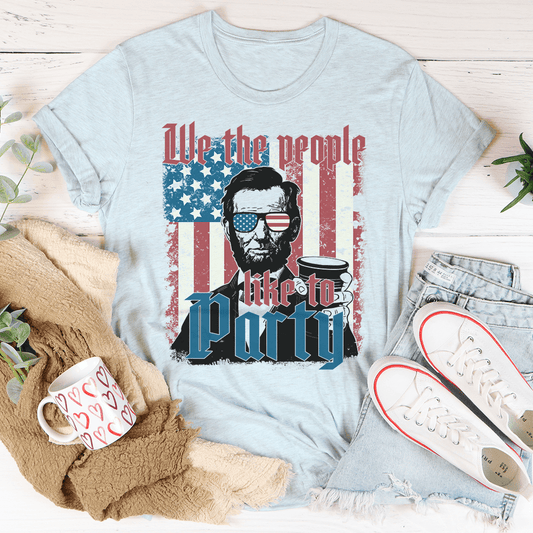 Light blue t-shirt with graphic of a historical figure and text 'We the people like to Party' on an American flag background.
