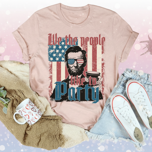 Pink t-shirt with graphic design featuring a person holding a coffee cup and American flag, surrounded by casual items.