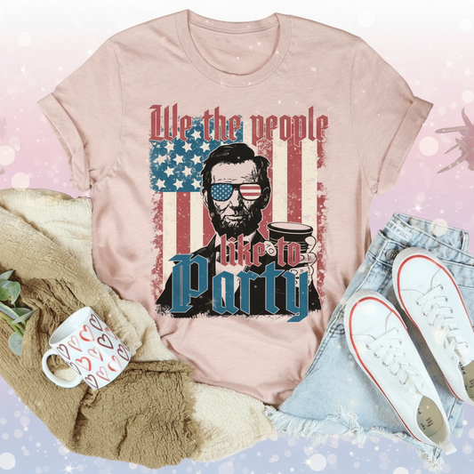 Pink t-shirt with graphic design featuring a person holding a coffee cup and American flag, surrounded by casual items.