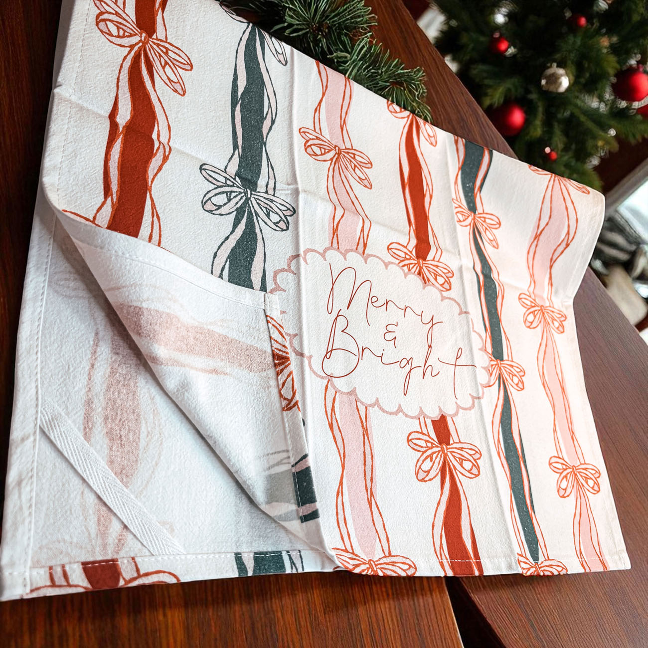 Decorative towel with candy cane pattern and 'Merry & Bright' text on a wooden surface with a Christmas tree in the background.