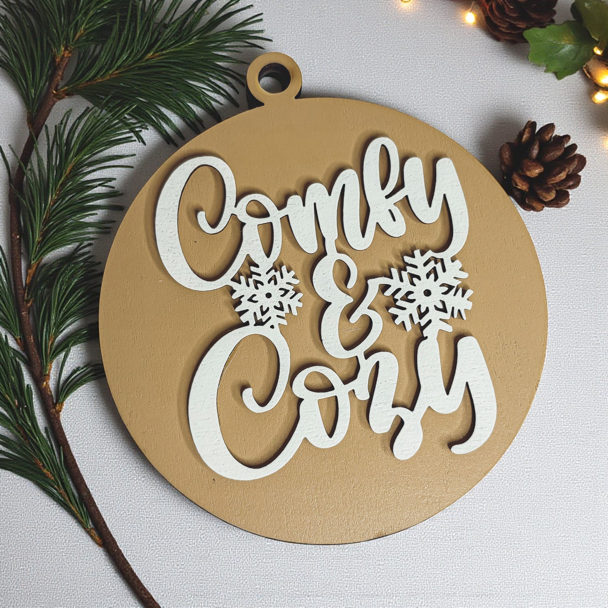 Decorative wooden ornament with 'Cozy & Cozy' text and snowflake designs on a white background.