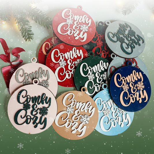 Decorative ornaments with 'Comfy & Cozy' text on a light background with Christmas decorations.