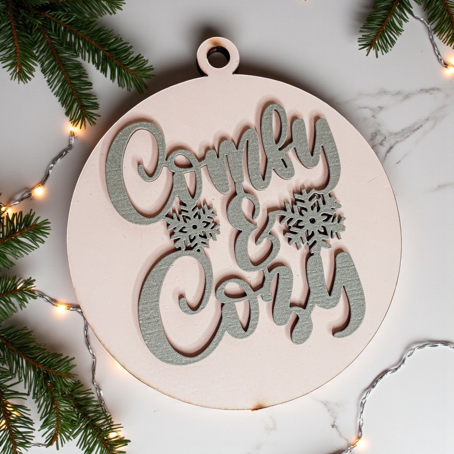 Decorative wooden ornament with 'Comfy & Cozy' text on a marble surface with Christmas decorations.
