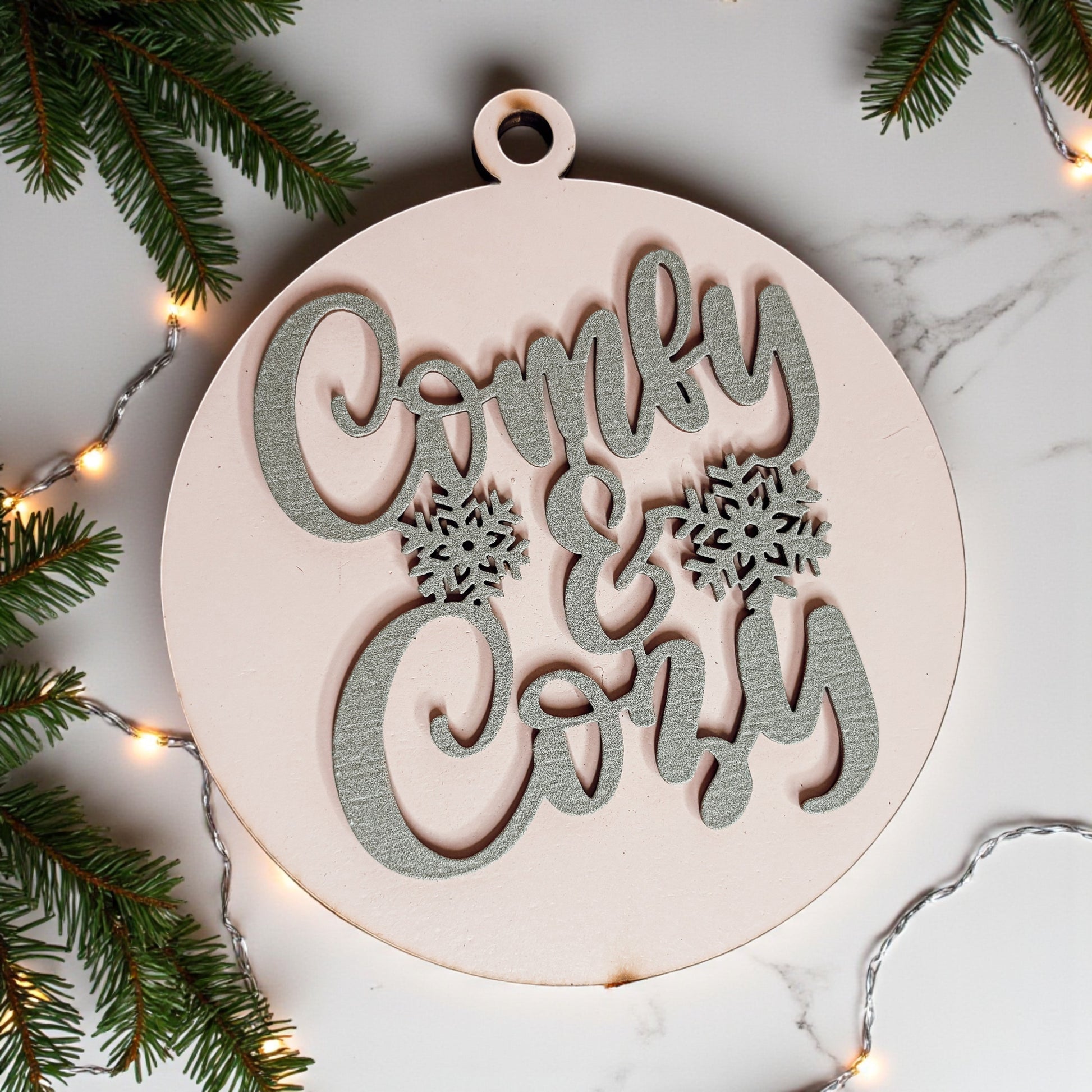 Decorative wooden ornament with 'Comfy & Cozy' text on a marble surface with Christmas decorations.
