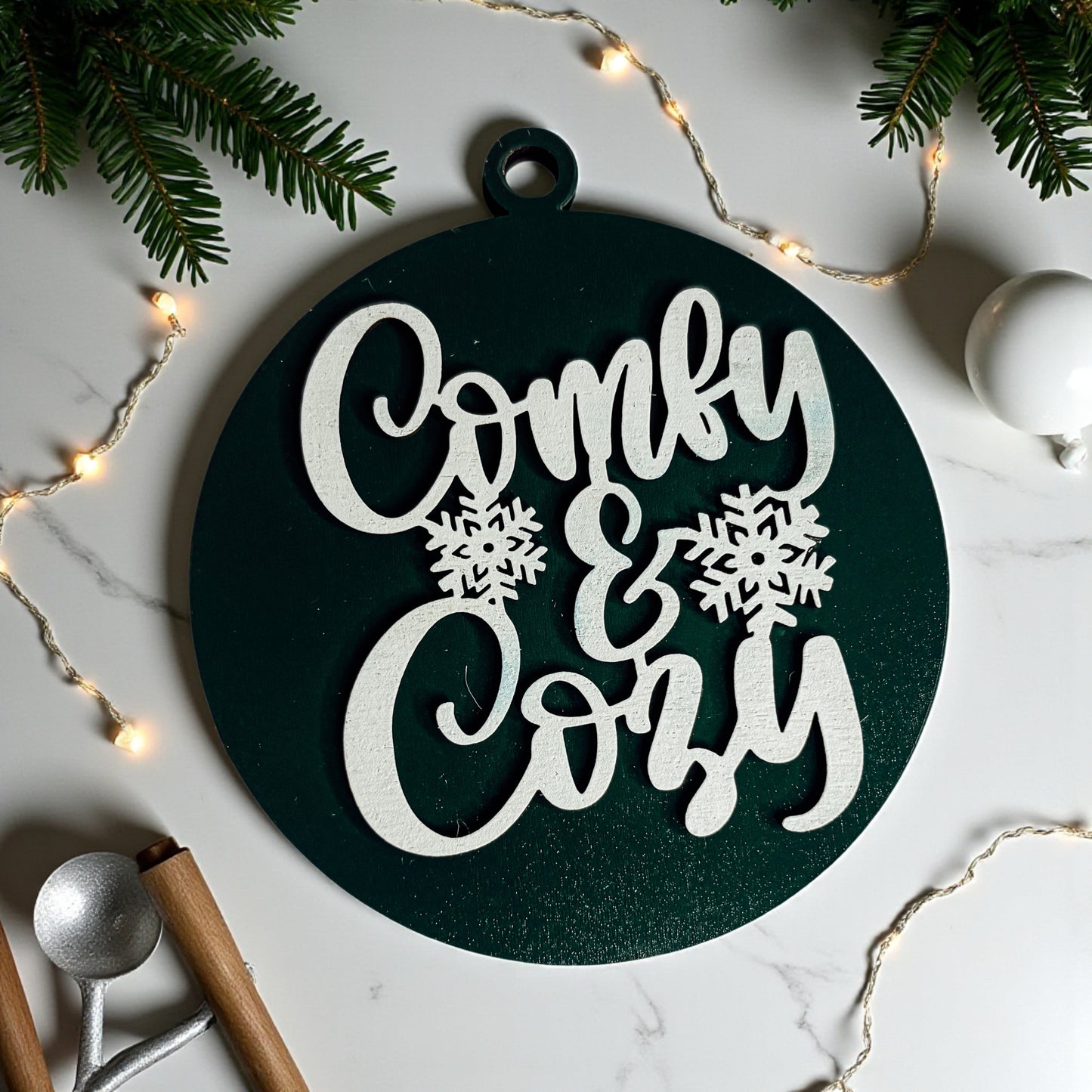 Decorative sign with 'Comfy & Cozy' text on a marble surface with Christmas decorations.