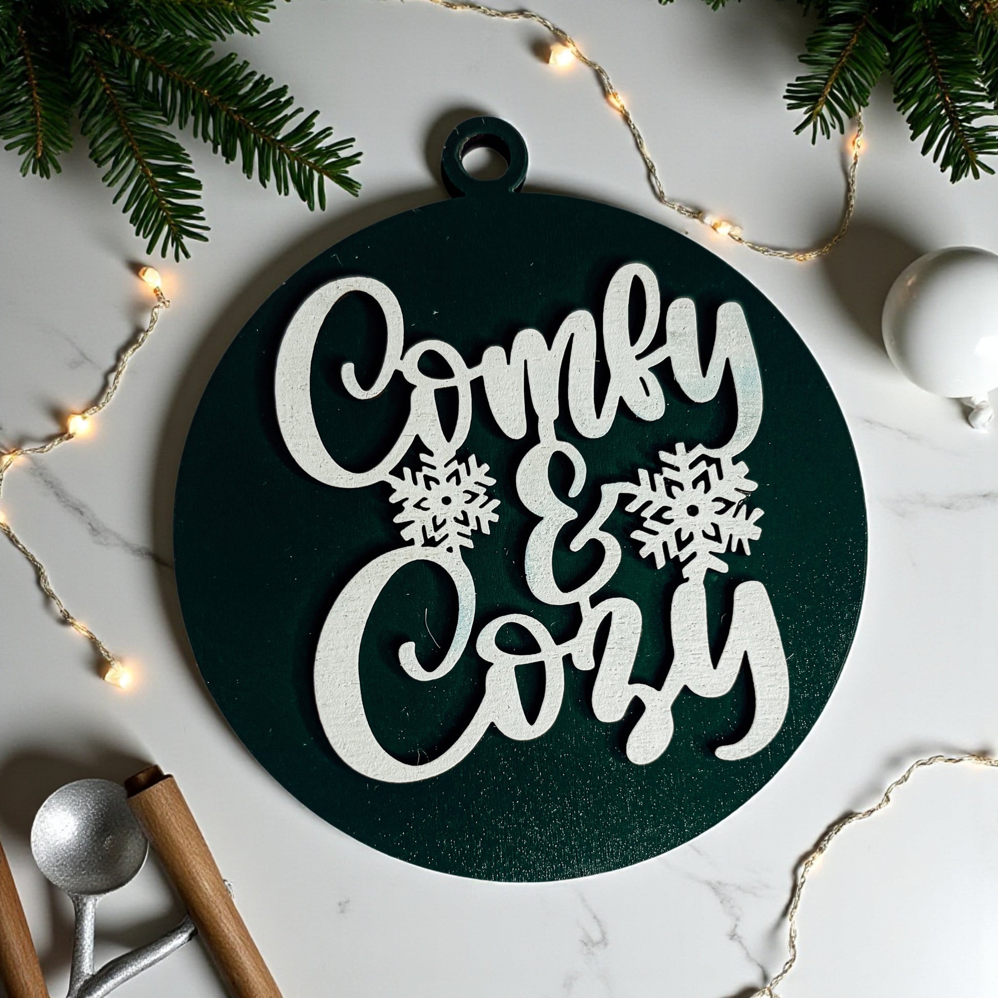 Decorative sign with 'Comfy & Cozy' text on a marble surface with Christmas decorations.