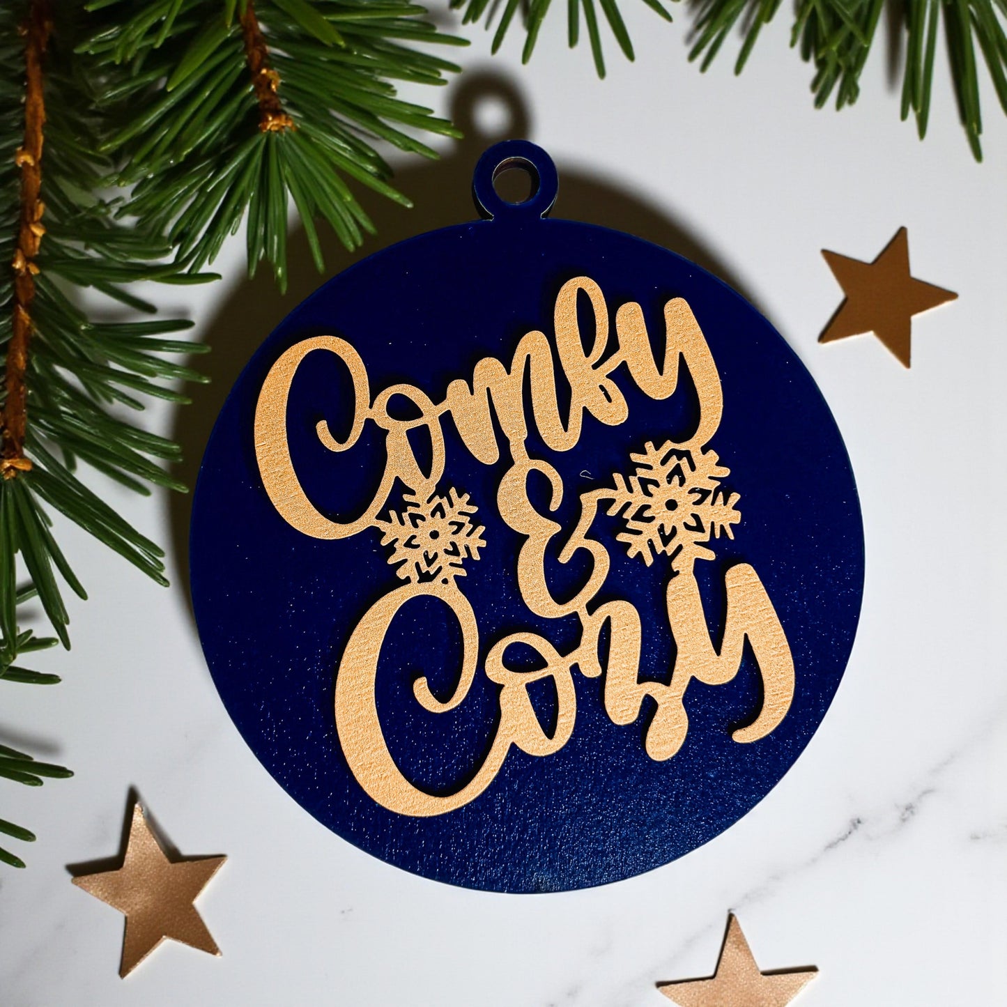 Decorative ornament with 'Comfy & Cozy' text on a blue background with Christmas trees and stars.