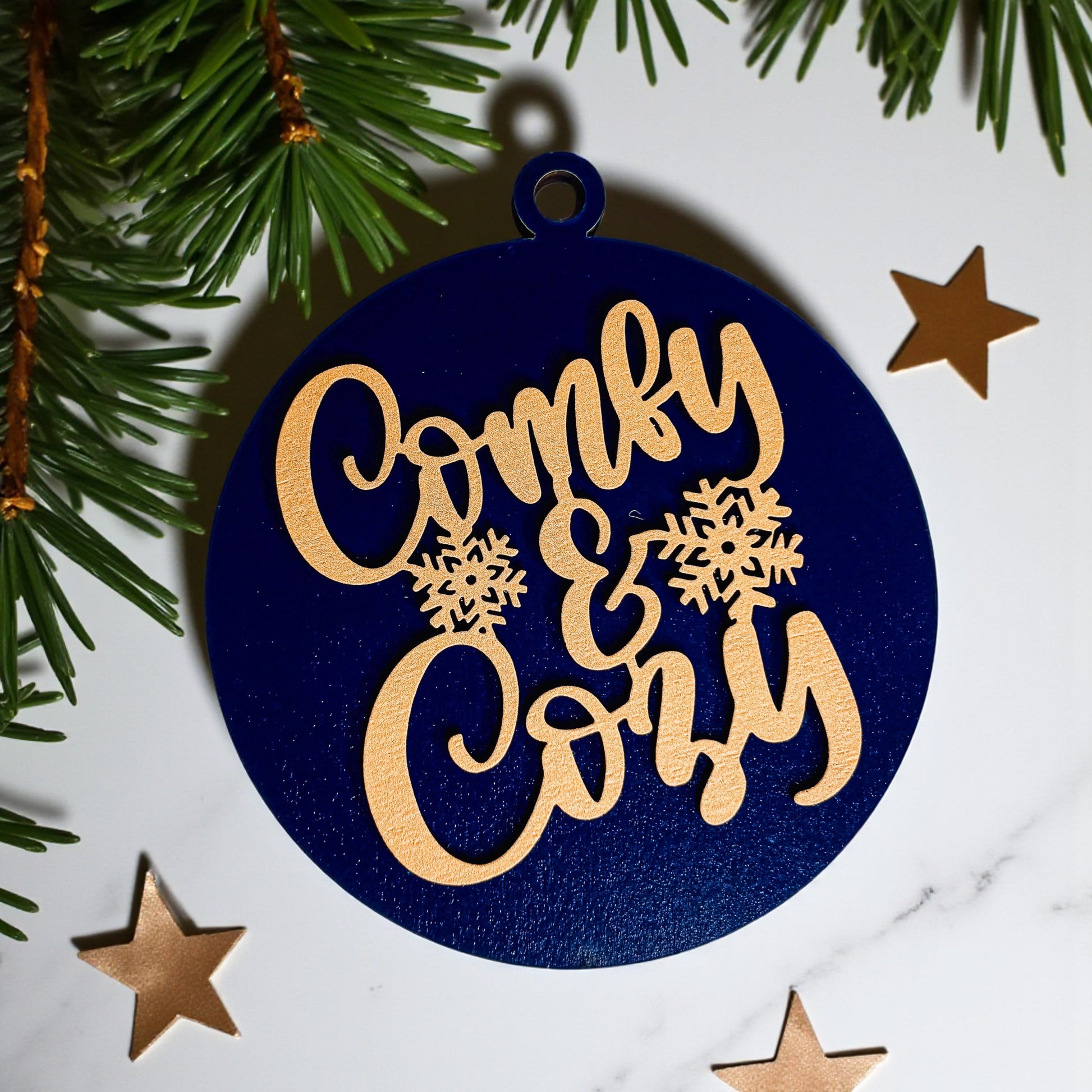 Decorative ornament with 'Comfy & Cozy' text on a blue background with Christmas trees and stars.
