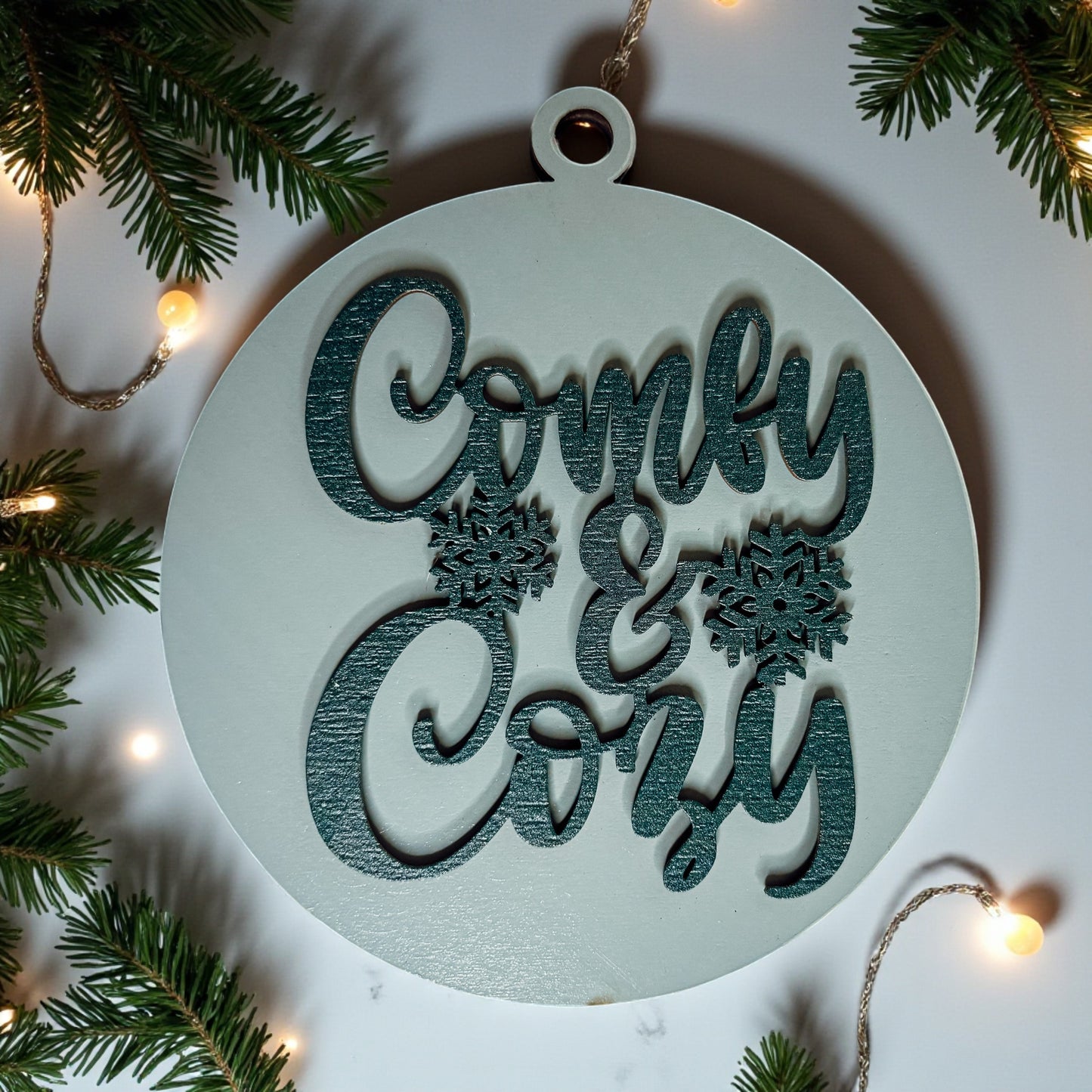 Decorative ornament with 'Comly & Cory' text surrounded by Christmas tree branches and lights.