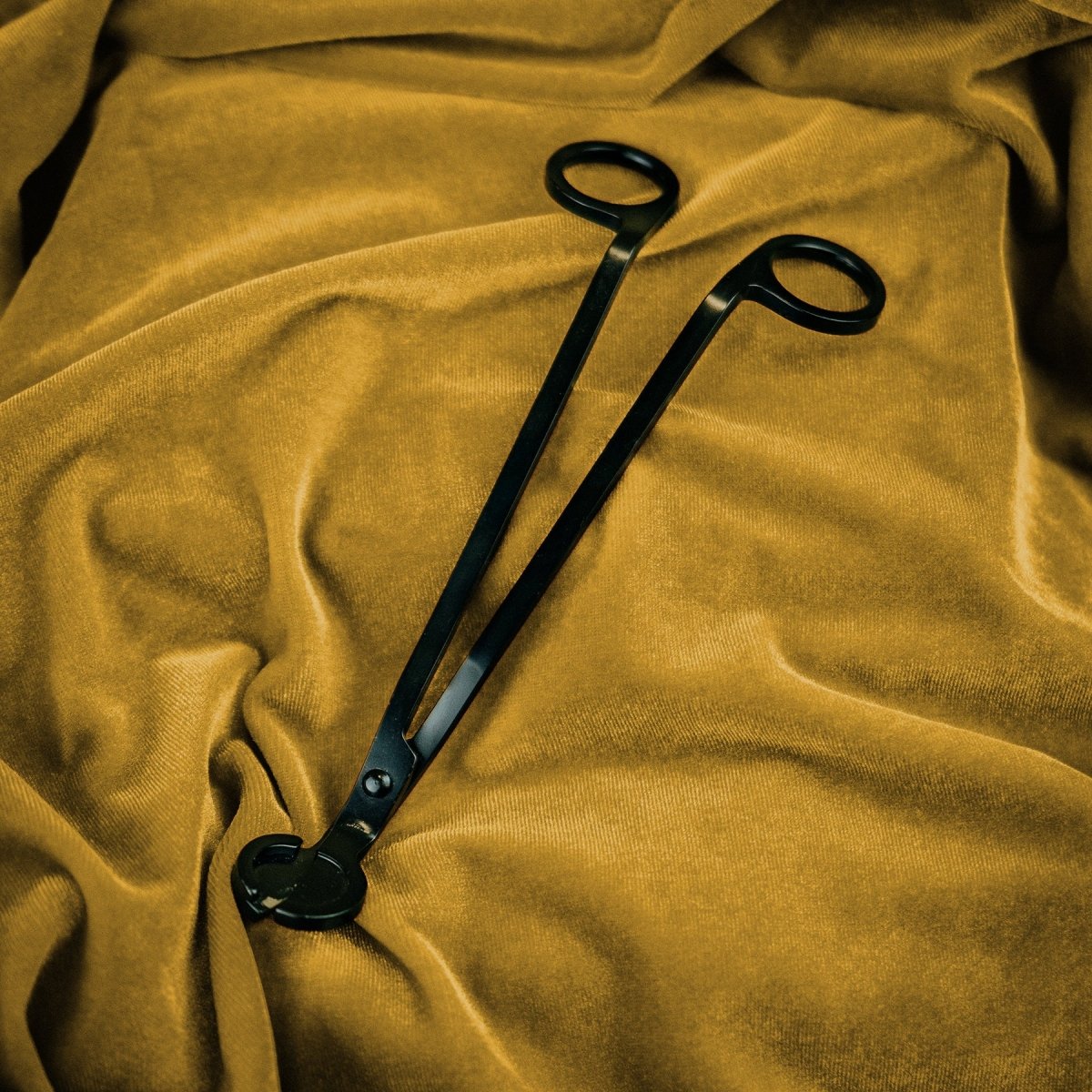 Black tongs on a textured mustard yellow fabric background