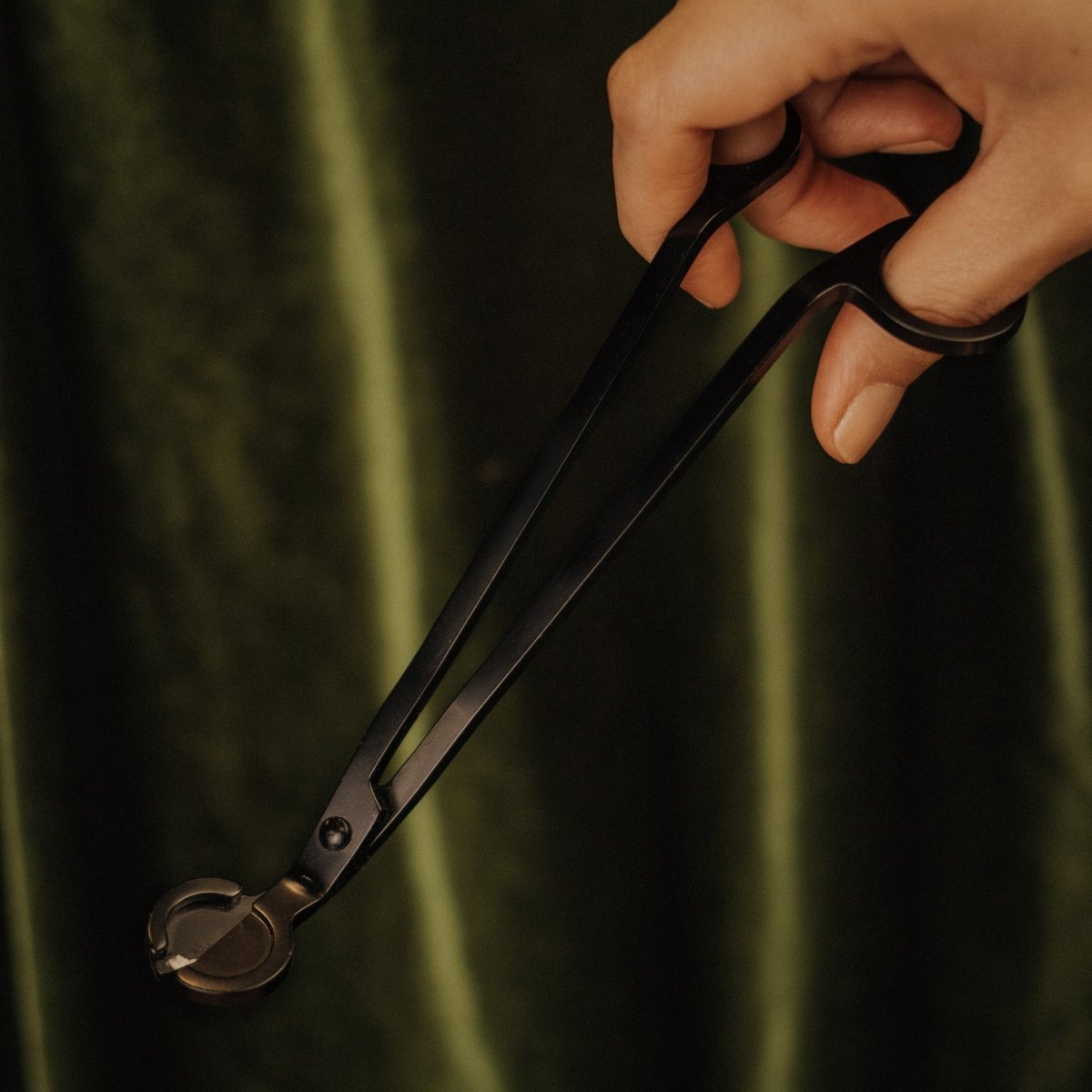 Hand holding a pair of black pliers against a dark background