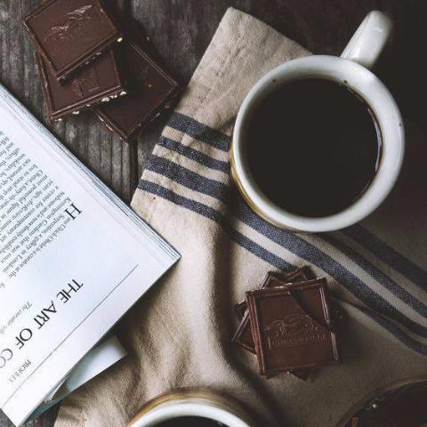 Cup of coffee, chocolate bars, and a book on a striped fabric surface