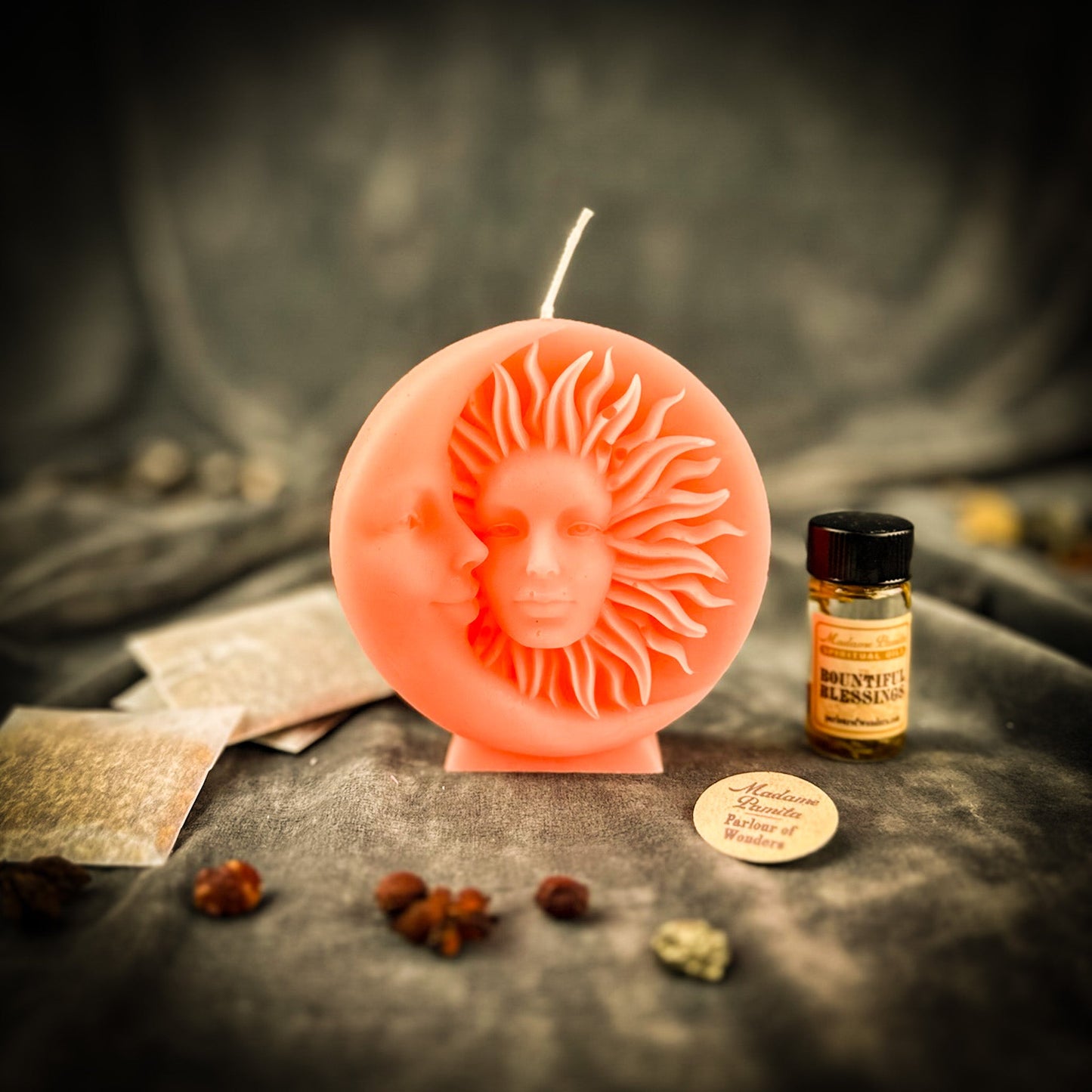 Decorative candle with face design on a dark surface with herbs and a bottle.
