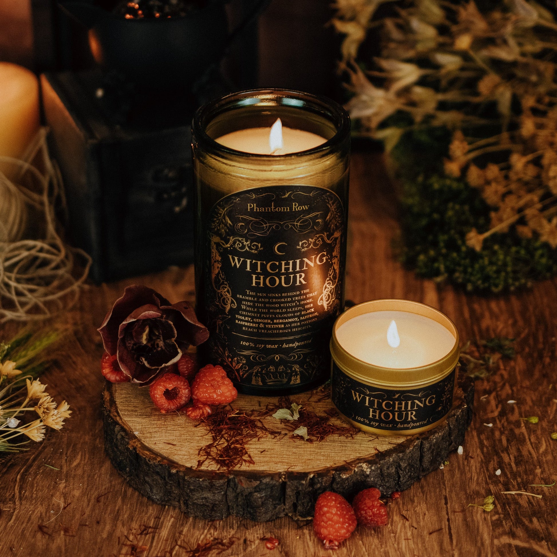 Two 'Witching Hour' candles on a wooden surface with dried flowers and berries.
