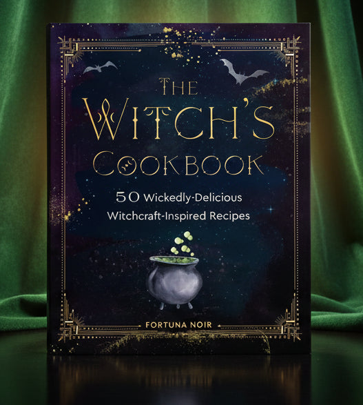 The Witch's Cookbook book cover by Fortuna Noir, featuring a dark starry night sky with bats, gold decorative border, and a cauldron with green potion bubbles. The title is written in large gold lettering.